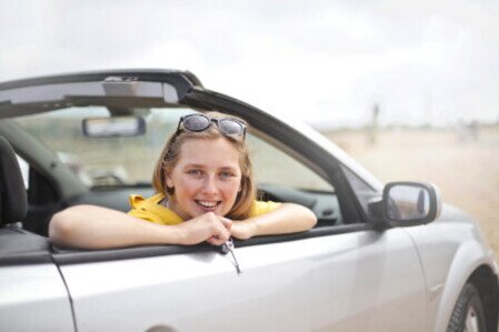 Junge Fahrschülerin sitzt im Auto und lächelt