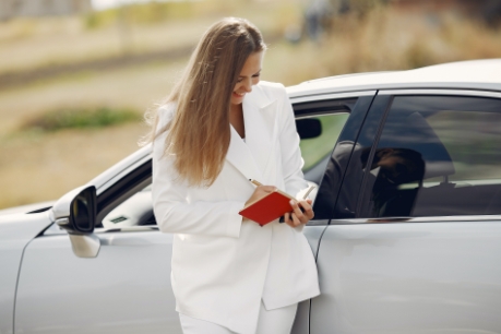 Junges Frau steht vor dem Auto mit Notizblock in der Hand